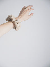 Image d'une main sur fond blanc, maxi chouchou couleur sable doux au poignet. Avec le logo de Marées - vêtements et essentiels d'allaitement