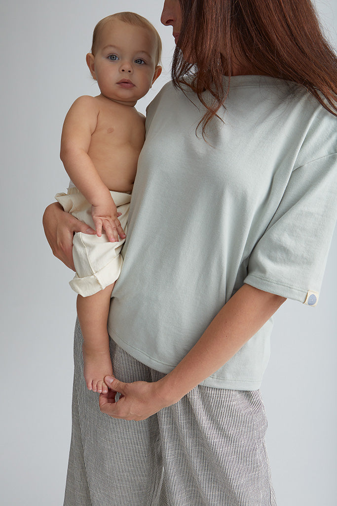 Maman debout avec bébé dans ses bras. Porte le tee-shirt box d'allaitement couleur seaglass. 