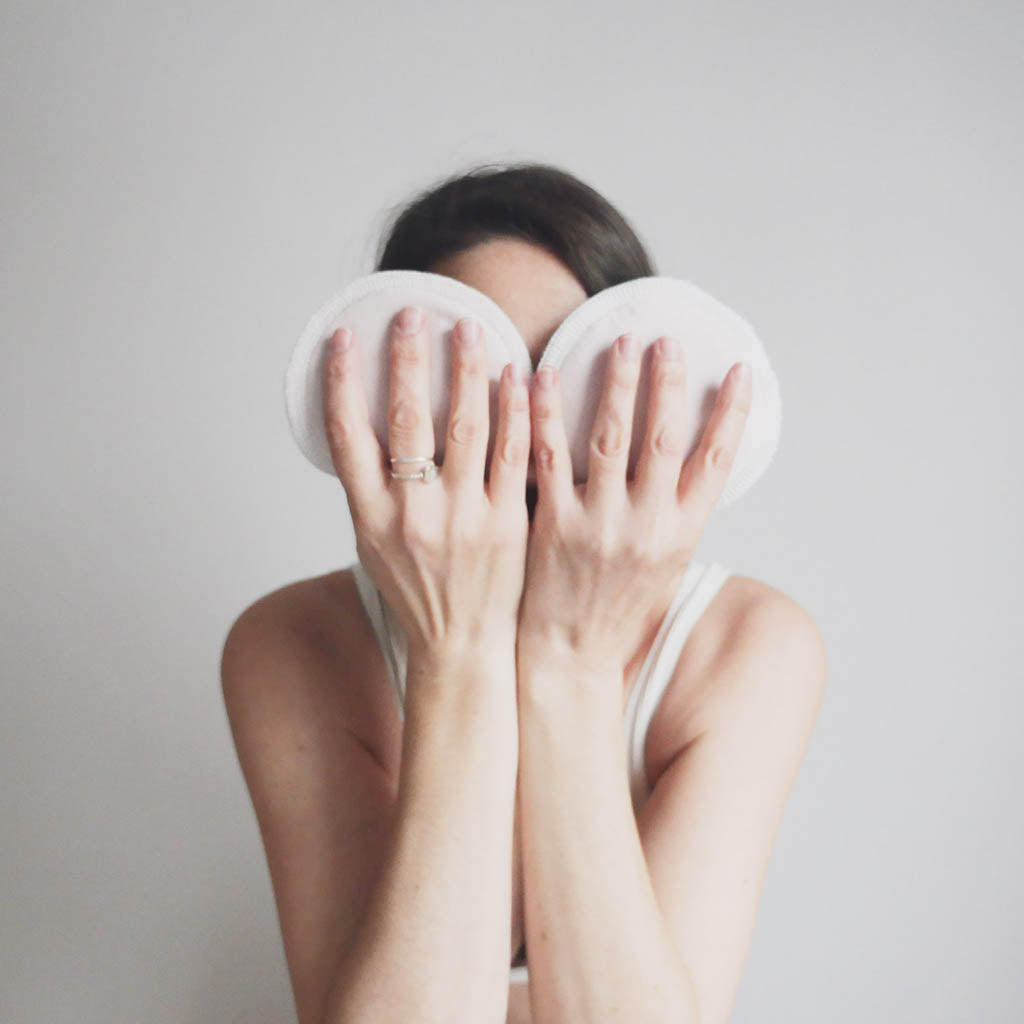 Femme qui cache son visage avec deux compresses d'allaitement en coton biologique.