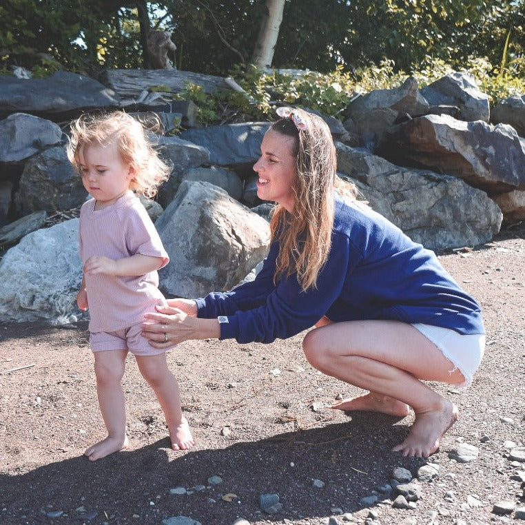Maman avec sa fille de 2 ans, portant le Sweatshirt Marées marine avec fermetures éclair latérales. Dehors, près des rochers. 
