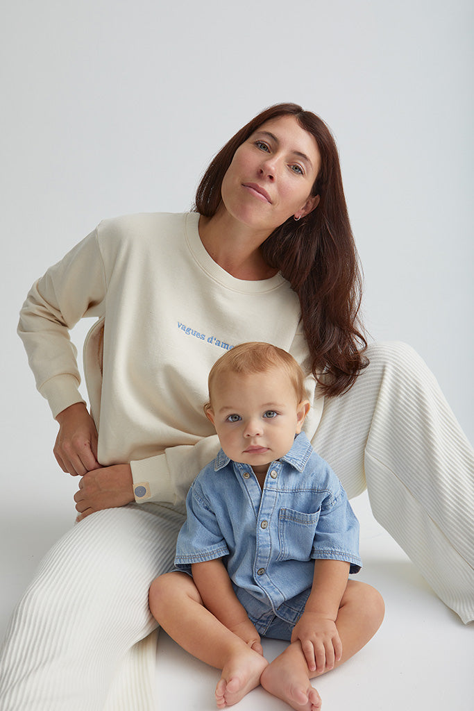 Maman assise avec bébé et qui ouvre zip et qui porte le crewneck d'allaitement Vagues d'amour