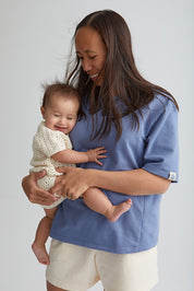 Maman qui tient bébé dans ses bras. Porte le tee-shirt box d'allaitement couleur bleu de mèr(e)