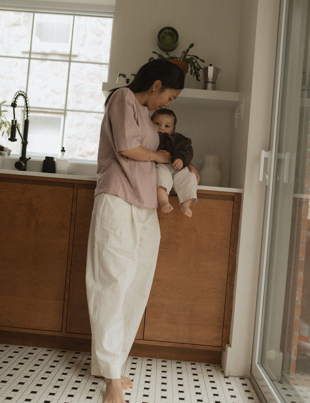 Maman dans la cuisine, avec bébé sur le comptoir, qui va allaiter bébé avec teeshirt d'allaitement Marées couleur Aube