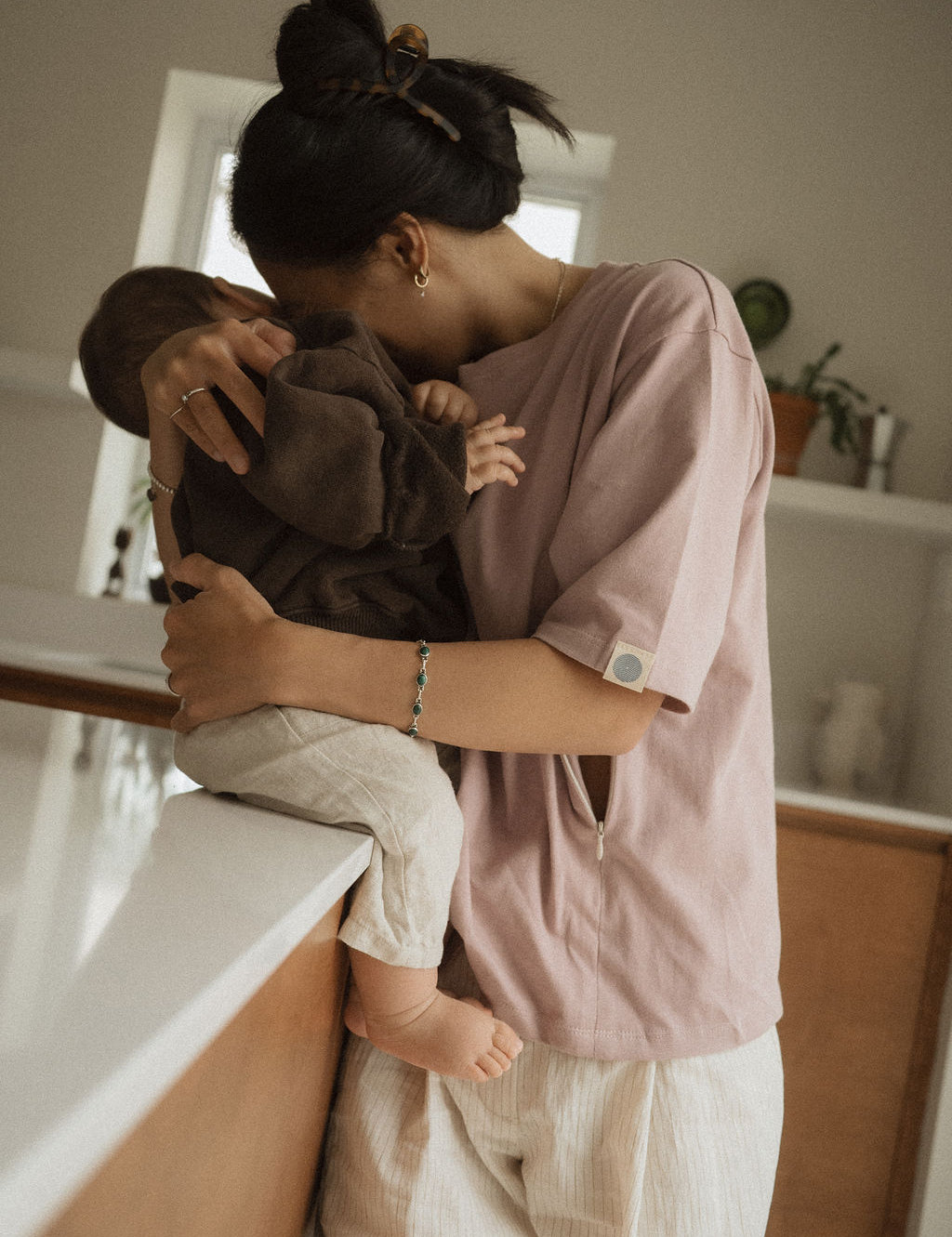 Maman dans la cuisine, avec bébé sur le comptoir, qui va allaiter bébé avec teeshirt d'allaitement Marées couleur Aube