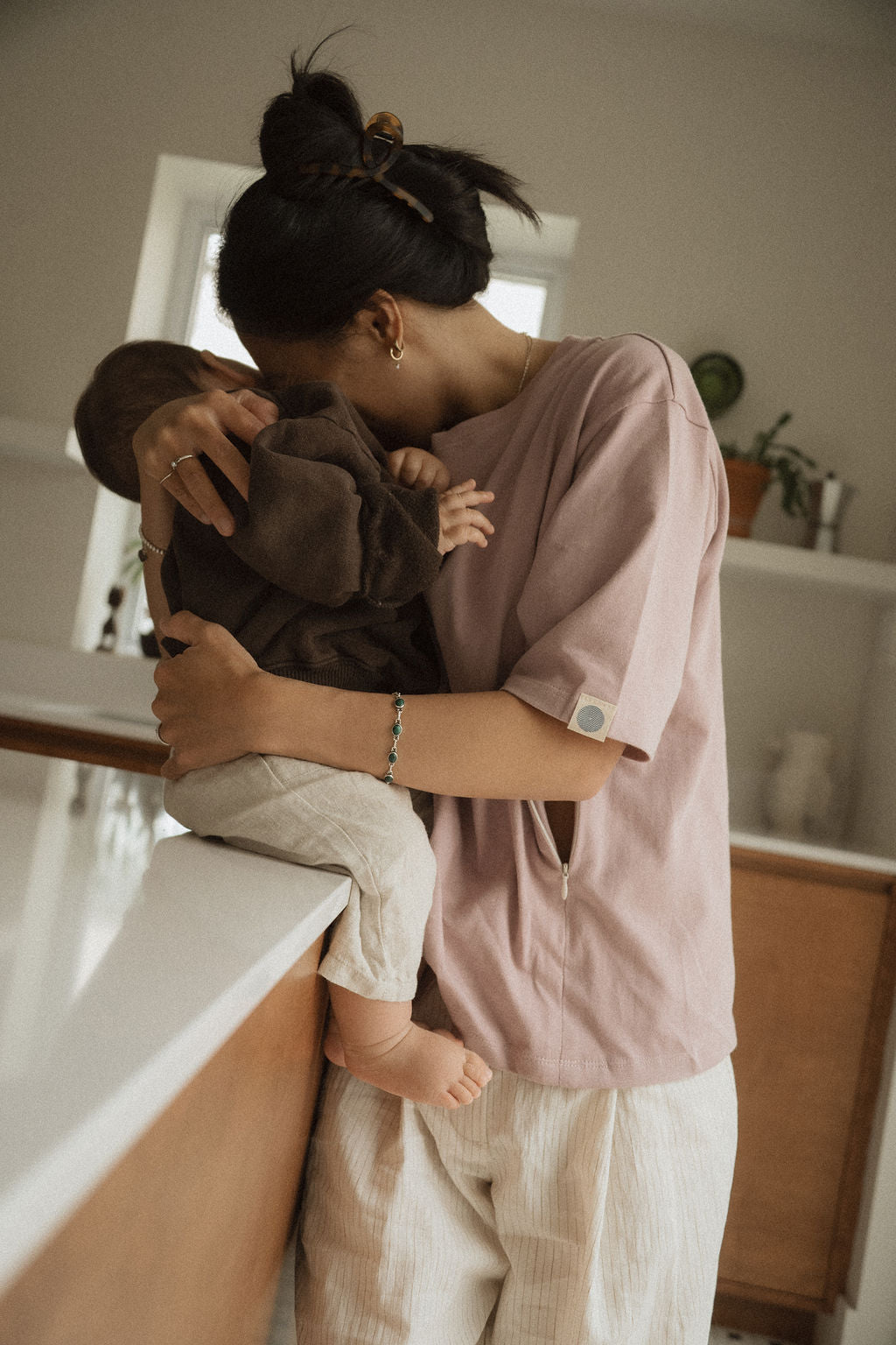 Maman dans la cuisine, avec bébé sur le comptoir, qui va allaiter bébé avec teeshirt d'allaitement Marées couleur Aube