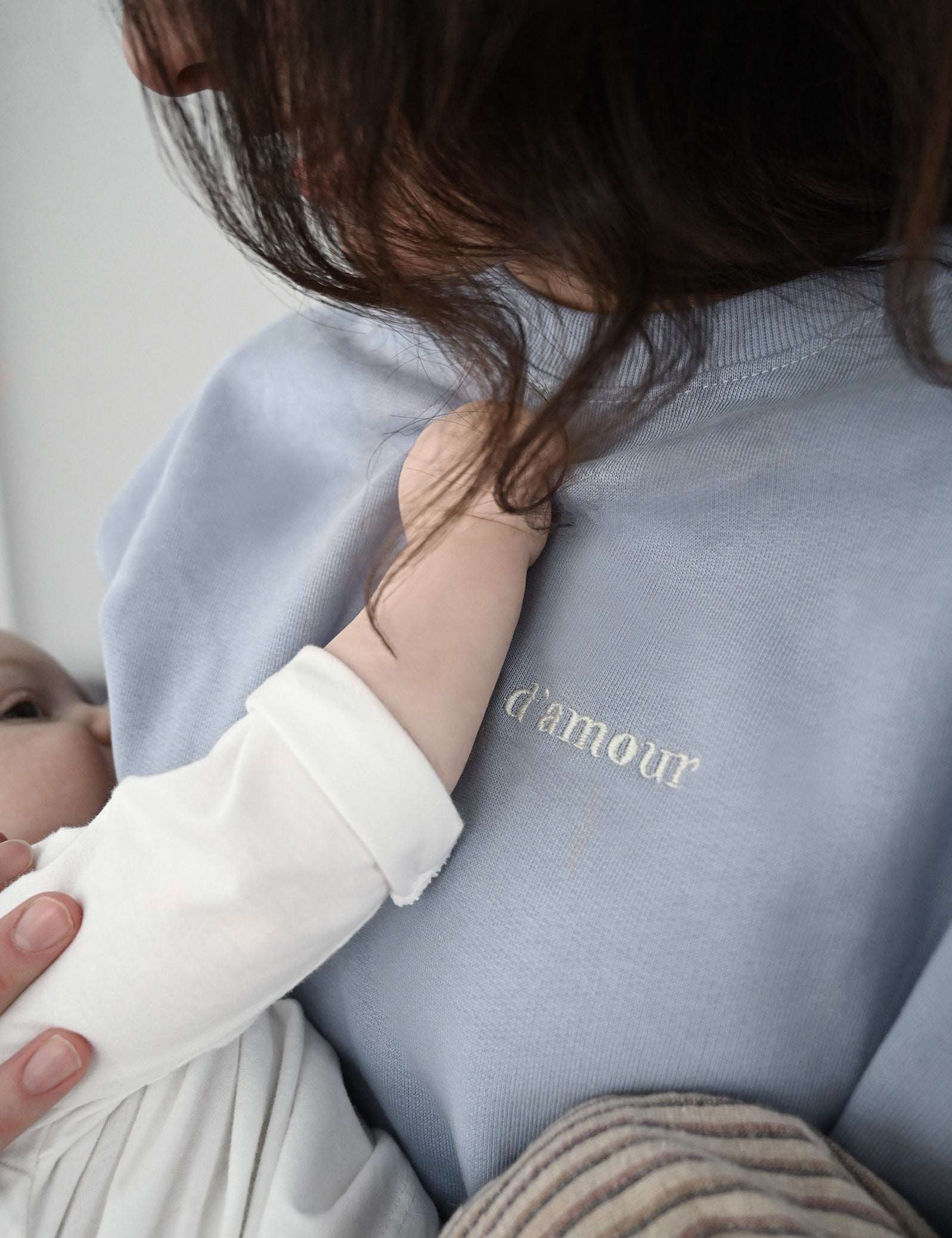 Gros plan sur Maman qui allaite bébé et crewneck d'allaitement Marées bleu ciel. Bébé tient le chandail. 