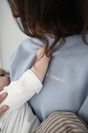 Gros plan sur Maman qui allaite bébé et crewneck d'allaitement Marées bleu ciel. Bébé tient le chandail. 