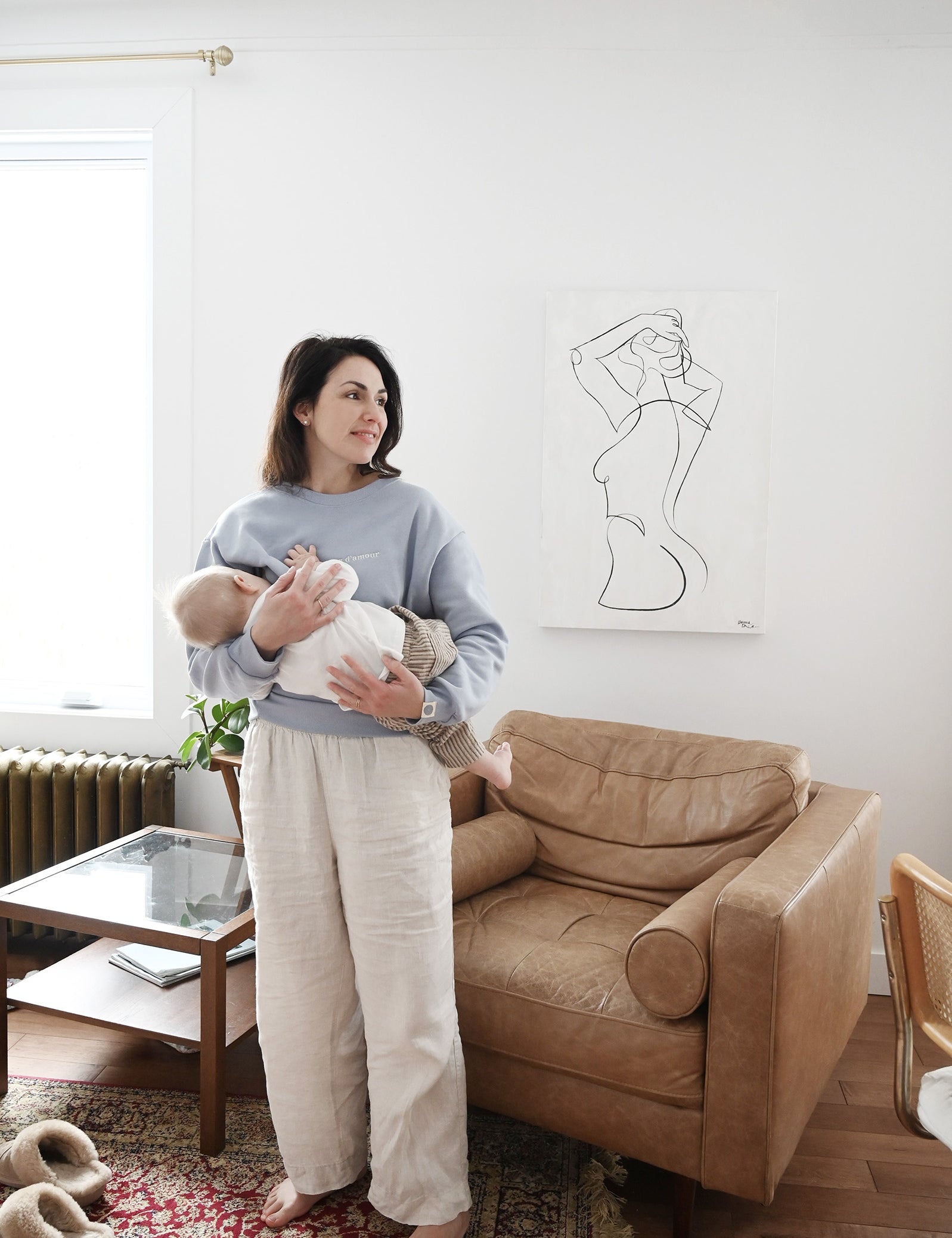 Maman dans son salon qui porte bébé debout et allaite avec crewneck d'allaitement Marées bleu ciel. 