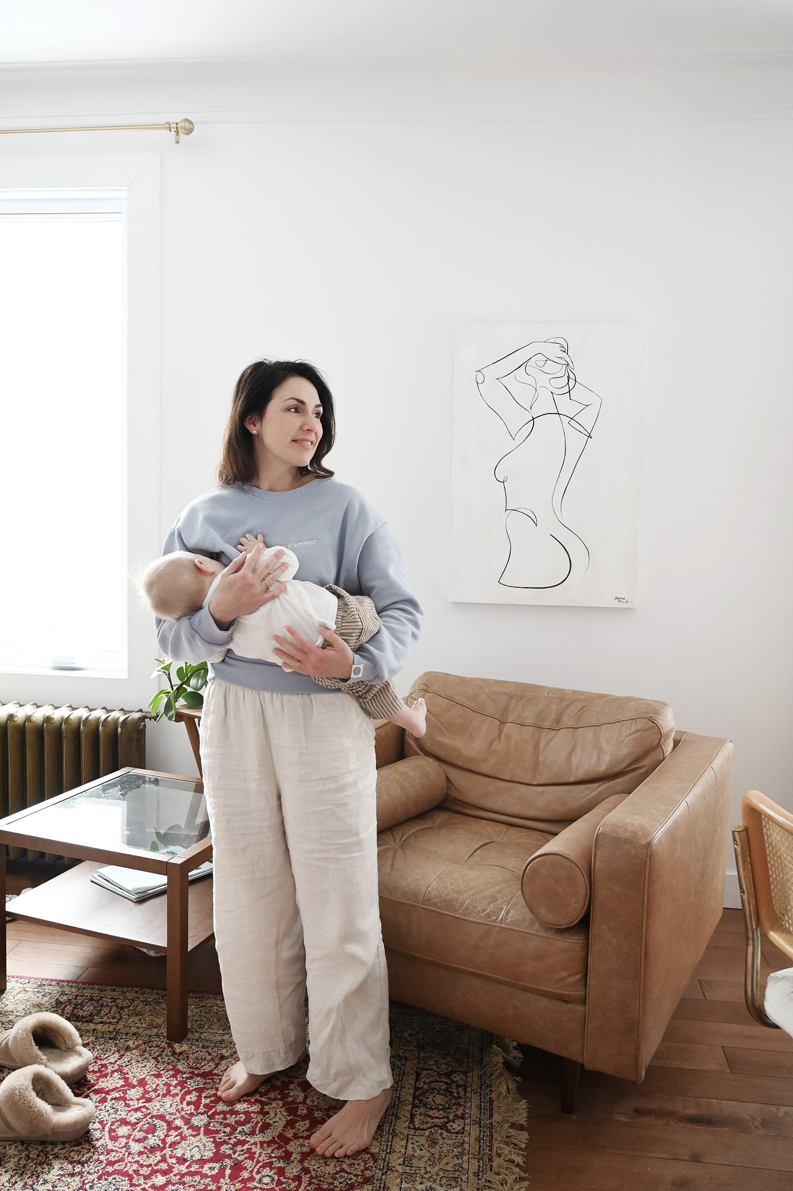 Maman dans son salon qui porte bébé debout et allaite avec crewneck d'allaitement Marées bleu ciel. 