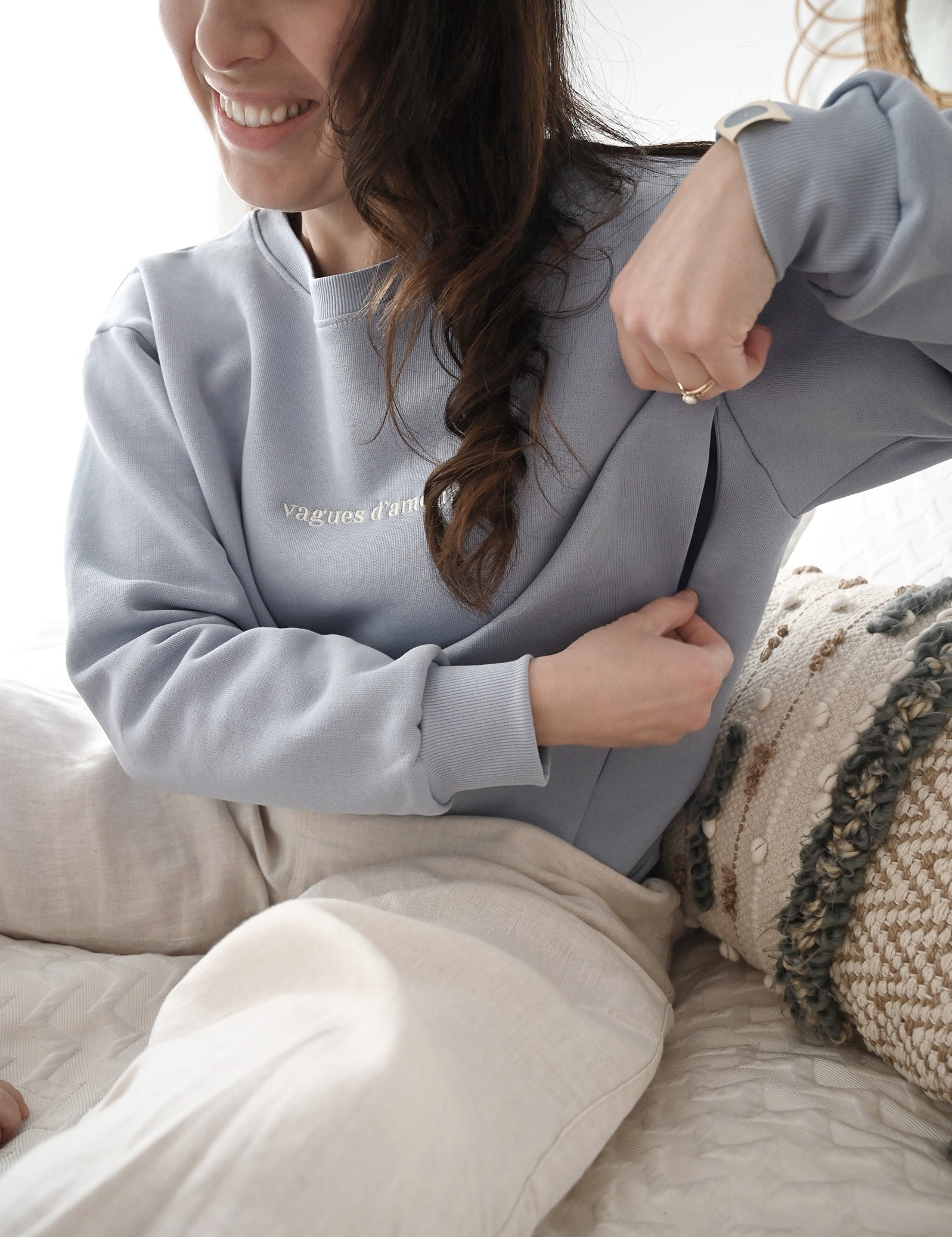 Maman sur son lit qui montre ouverture avec zip de son crewneck d'allaitement Marées bleu ciel. 