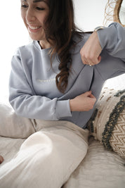 Maman sur son lit qui montre ouverture avec zip de son crewneck d'allaitement Marées bleu ciel. 