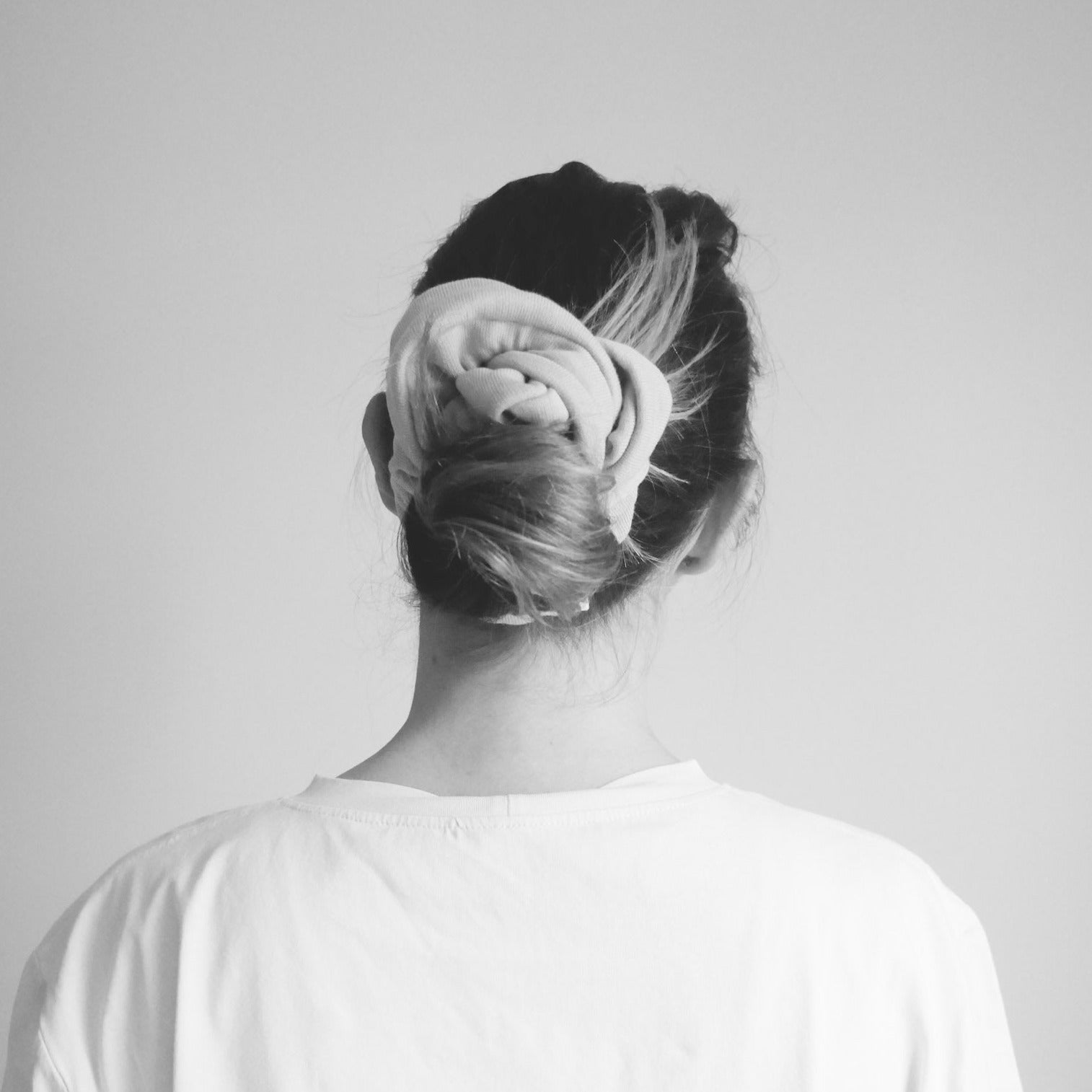 Femme de dos, avec un chignon fait avec un chouchou couleur sable doux. Photo en noir et blanc. 